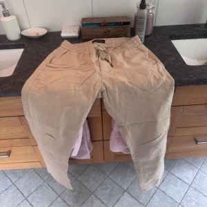 Beiga linnebyxor med snörning - Snygga beiga linnebyxor med avslappnad passform och elastisk midja med snörning. Perfekta för en chill och stilren look. Lätta och luftiga, passar grymt till sommaren eller våren.