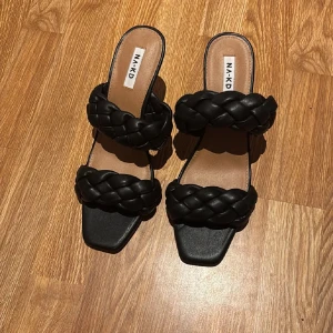 Svarta flätade klack-sandaler NA-KD - Stilrena svarta sandaler från NA-KD med två breda, flätade remmar och fyrkantig tå. Skorna har en smal klack och öppen häl, vilket ger en trendig look. Tillverkade i syntetmaterial med en elegant finish. Tryck ej köp nu