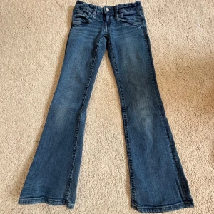 Blå bootcut jeans med klassisk tvätt - Snygga blå jeans med bootcut passform och klassisk femficksdesign. Jeansen har en lätt tvättad look och är tillverkade i mjukt denimtyg. Perfekta för dig som gillar en retroinspirerad stil med utsvängda ben.