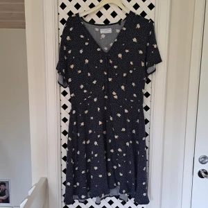 Blommig kortklänning från Holly & White - Supersöt marinblå kortklänning med vita små blommor från Holly & White. Klänningen har v-ringning, korta ärmar och ett flowy fall. Perfekt för sommarens alla tillfällen! Materialet känns lätt och svalt.