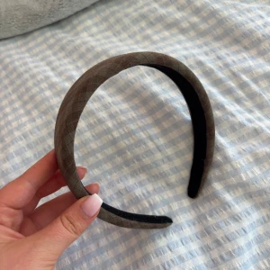 Brunt rutigt Diadem - Snyggt diadem i brunt tyg med diskret rutigt mönster. Bred och vadderad modell som sitter bekvämt på huvudet och ger en stilren touch till din look. Perfekt accessoar för att lyfta vilken outfit som helst.