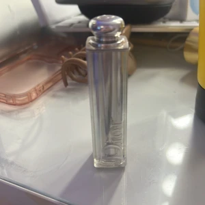Dior läppstift rosa-nude - Säljer ett lyxigt läppstift från Dior i en snygg rosa-nude nyans. Hylsan är transparent med silverdetaljer och har Dior-loggan ingraverad. Perfekt för dig som vill ha en elegant och klassisk look med en hint av färg.