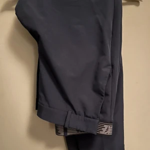 Mörkblå Dri-FIT byxor från Nike - Snygga mörkblå byxor från Nike med Dri-FIT-teknologi och elastisk midja med ränder. Perfekta för träning eller sportiga tillfällen. Byxorna har en bakficka och är tillverkade i ett syntetmaterial som andas.