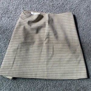 Rutig kjol från H&M - Säljer en snygg rutig kjol från H&M i beige och svart. Kjolen har klassiskt hundtandsmönster och dragkedja i sidan. Perfekt för dig som gillar en stilren och tidlös look. Modellen är rak och kort. Kjolen är insydd begrund utav att den inte passade innan men det går självklart att sprätta upp. Kjolen är i storlek 170 innan vi sydde in den men ör nu i storlek 152-158