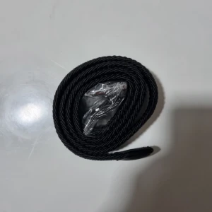Grå grisch belte - Säljer ett grå flätat bälte med snygg läderdetalj vid änden. Bältet har en stilren design och passar perfekt till jeans eller byxor. Enkel att justera för bästa passform.