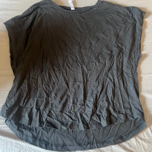 Mörkgrå t-shirt från kay/day - En enkel mörkgrå t-shirt från kay/day med rund halsringning och korta ärmar. Modellen är lite längre baktill och har en avslappnad passform. Perfekt till vardags och lätt att matcha med andra plagg.