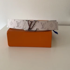 Vit Louis Vuitton bälte med monogram - Säljer ett vitt Louis Vuitton bälte med klassiskt monogrammönster och silverfärgat LV-spänne. Bältet är i skinn och levereras med originalförpackning, dustbag & påse.