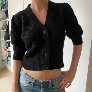 Svart croppad kofta med knappar - Säljer en svart croppad kofta med trekvartsärm och stora knappar framtill. Tröjan har tappat en av knapparna.