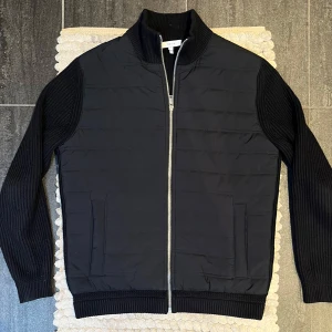 Reiss Cardigan Hybrid Jacka Navy - Stilren cardigan/hybridjacka från Reiss i mörkblått, storlek M. Mycket fint skick – enda anmärkningen är att storlekslappen i nacken delvis lossnat. Perfekt som lager på lager-plagg eller lätt jacka på vår och höst.