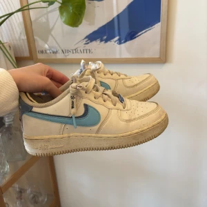 Nike Air Force 1 med blå swoosh - Säljer ett par klassiska Nike Air Force 1 med vit bas och ljusblå detaljer! Storlek 36,5