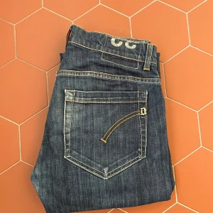 Mörkblå Dondup jeans - Säljer ett par mörkblå Dondup jeans med raka ben och slitna detaljer på båda knäna. Jeansen har kontrastsömmar, klassiska fem fickor och knappgylf. Perfekta för en avslappnad och trendig look. Priset kan diskuteras!😎