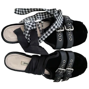 Miu Miu sandaler - Unika svarta sandaler från Miu Miu med dubbla spännen och silvriga nitar. Skorna har rutiga och svarta band som kan knytas runt vristen för en cool look. Perfekta för dig som vill sticka ut med detaljer och mönster.