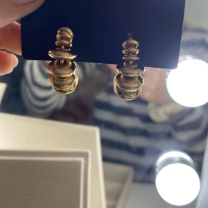 Chunky guldörhängen i spiralform - Säljer ett par statement örhängen i guld med chunky, spiralformad design. Örhängena har en unik och modern look med flera ovala, glänsande delar som bildar en cirkel. Perfekta för att lyfta vilken outfit som helst! 