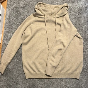 Beige stickad hoodie av kachmir  - Mysig beige stickad hoodie med dragsko i huvan. Tröjan har långa ärmar och ribbade muddar vid ärmslut och nederkant. Perfekt för lager-på-lager och chill dagar.