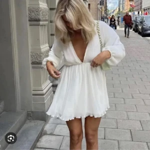 Vit kortklänning Na-kd - Superfin vit eftertraktad kortklänning med djup v-ringning och långa ballongärmar. Klänningen har knytning i ryggen och ett luftigt, flowy tyg som ger en somrig känsla. Perfekt för sommarens alla tillfällen. Säljer pga att den var för stor. Pris går att diskutera.