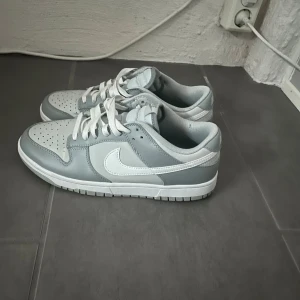 Nike Dunk Low sneakers i vitt och ljusgrått - Säljer ett par Nike Dunk Low sneakers i vitt och ljusgrått. Skorna har bara blivit använda någon enstaka gång och är i bra skick!