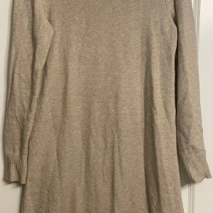 Beige stickad klänning - Mysig beige stickad klänning med lång ärm och rund hals. Perfekt för kyligare dagar och enkel att styla med boots eller sneakers. Ribbstickade muddar vid ärmslut och nederkant ger en snygg detalj.