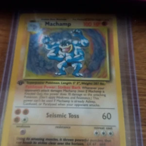 Machamp Pokémonkort 1st Edition - Säljer ett Machamp Pokémonkort från 1st Edition. Kortet har en gul ram, holografisk bild på Machamp och attacken Seismic Toss. Perfekt för samlare eller Pokémonfans som vill utöka sin samling.
