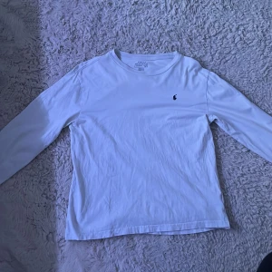 Vit långärmad tröja från Polo Ralph Lauren - Säljer en klassisk vit långärmad tröja från Polo Ralph Lauren med den ikoniska broderade loggan på bröstet. Tröjan har rund halsringning och är tillverkad i mjuk bomull, perfekt för en stilren och enkel look. Tröjan är storlek S men den har krympt lite och är typ mer som en xs.
