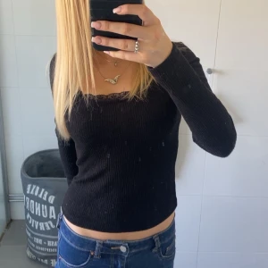 Svart ribbad långärmad topp - Säljer en svart ribbad långärmad topp med croppad passform och fin v-ringning med spetsdetalj vid halsen. Perfekt att matcha med jeans eller kjol för en snygg look 💕