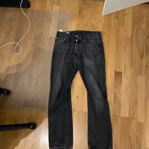 Svarta Levi's 501 jeans - Klassiska svarta Levi's 501 jeans med raka ben och knappgylf. Jeansen har en tidlös design och är tillverkade i slitstarkt denim. Perfekta för dig som gillar en ikonisk och enkel stil. Midjemått W31 och längd L32.