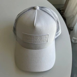 Vit meshkeps från Mitchell & Ness - Snygg vit keps från Mitchell & Ness med mesh på sidorna och justerbar snapback baktill. Framsidan har en diskret broderad logotyp i vitt. 