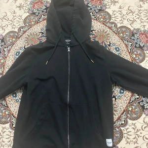 Svart hoodie med dragkedja från Jack & Jones - Säljer en svart hoodie från Jack & Jones i storlek M. Tröjan har dragkedja framtill, huva med snörning och två fickor. Perfekt för en avslappnad stil och enkel att matcha med det mesta. Pris kan såklart diskuteras