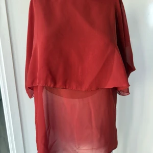 Röd transparent tunika från Vila - Säljer en röd, luftig och transparent tunika från Vila. Klänningen har ett lager på lager-utseende och är tillverkad i ett tunt, lätt material som ger ett flowy intryck. Perfekt för varma dagar eller som strandklänning.