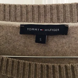 Beige tröja från Tommy Hilfiger - Säljer en stilren beige tröja från Tommy Hilfiger. Tröjan har långa ärmar och ribbade detaljer vid hals, ärmslut och nederkant. Perfekt för en avslappnad och snygg look.