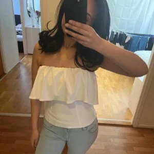 Vit offshoulder topp - Säljer en stilren vit offshoulder topp med volangdetalj. Perfekt för sommarens varma dagar. Passar bra till både jeans och kjol. Andvänd 2 ggr