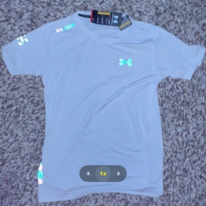 Vit träningst-shirt från Under Armour - Säljer en vit kortärmad t-shirt från Under Armour, modell HeatGear. Perfekt för träning med lätt och andningsbart material som håller dig torr och sval. Klassisk passform med diskret logga på bröstet och tryck på ärmen.