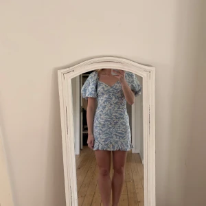 Klänning - Säljer en söt blå klänning med vita blommor och puffiga kortärmar. Klänningen har en volangdetalj vid fållen och en v-ringad hals. Perfekt för sommarens alla tillfällen! Pris kan diskuteras 