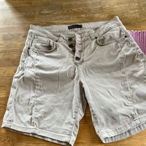 Beige shorts med knappar från object - Snygga beige shorts från object med flera knappar framtill och klassiska fickor både fram och bak. Modellen har normal passform och är tillverkad i ett mjukt bomullsmaterial. Perfekta för varma dagar och enkel att matcha med olika toppar.