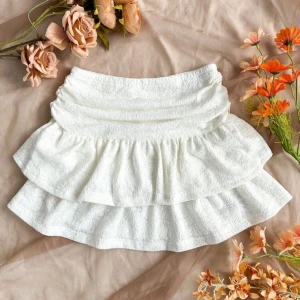 Vit volangkjol med blommönster -  vit kjol med volanger och blommönster. Perfekt för en somrig look. Kjolen har en kort längd och är tillverkad i ett lätt och luftigt material.