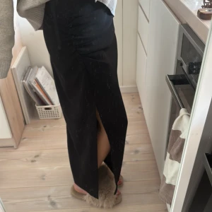 Svart långkjol med slits - Snygg svart långkjol med en elegant slits på sidan. Kjolen har en stilren design och passar perfekt för olika tillfällen. Den är gjord i ett mjukt och bekvämt material som ger en fin passform.