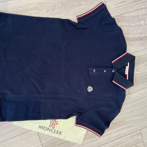 Moncler piké - Klassisk mörkblå pikétröja frän Moncler i nytt skick. Köpt på plick så kan ej garantera äkthet. Priset är inte hugget i sten, bara att skriva vid fragor.