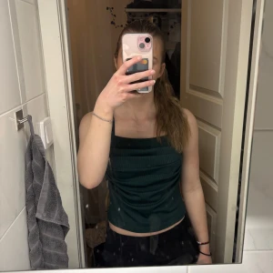 Mörkgrön ärmlös topp - Snygg mörkgrön ärmlös topp med en stilren design. Perfekt för en kväll ute eller en avslappnad dag. Toppen har en figurnära passform och är tillverkad i ett mjukt material.