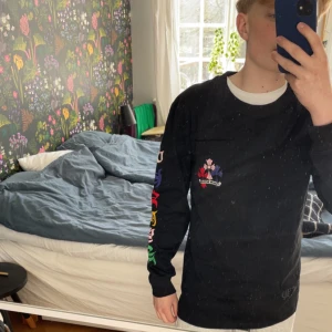 Svart långärmad tröja med blommigt mönster - Säljer en svart långärmad tröja med färgglada blommor på ärmarna och bröstet. Perfekt för en stilren och unik look. Tröjan har en normal passform och är tillverkad i ett mjukt material.