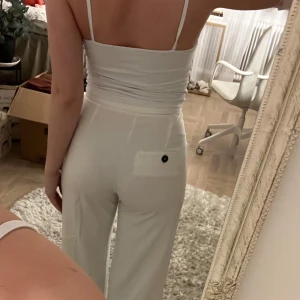 Vita kostymbyxor från Bershka - Säljer ett par vita kostymbyxor från Bershka med normal passform. Byxorna har hög midja, raka ben och en bakficka med knapp. Perfekta för en stilren look och lätta att matcha med olika toppar.