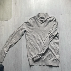 Beige tröja från Dressmann - Säljer en stilren beige tröja från Dressmann. Tröjan har en ribbad krage och långa ärmar med ribbade muddar. Perfekt för en avslappnad men ändå snygg look.