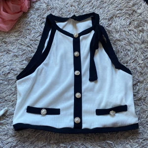 Vit och svart topp med knyt - Snygg vit topp med svarta detaljer och knytband vid halsen. Toppen har dekorativa knappar framtill och två små fickor. Passar både S & M.💖
