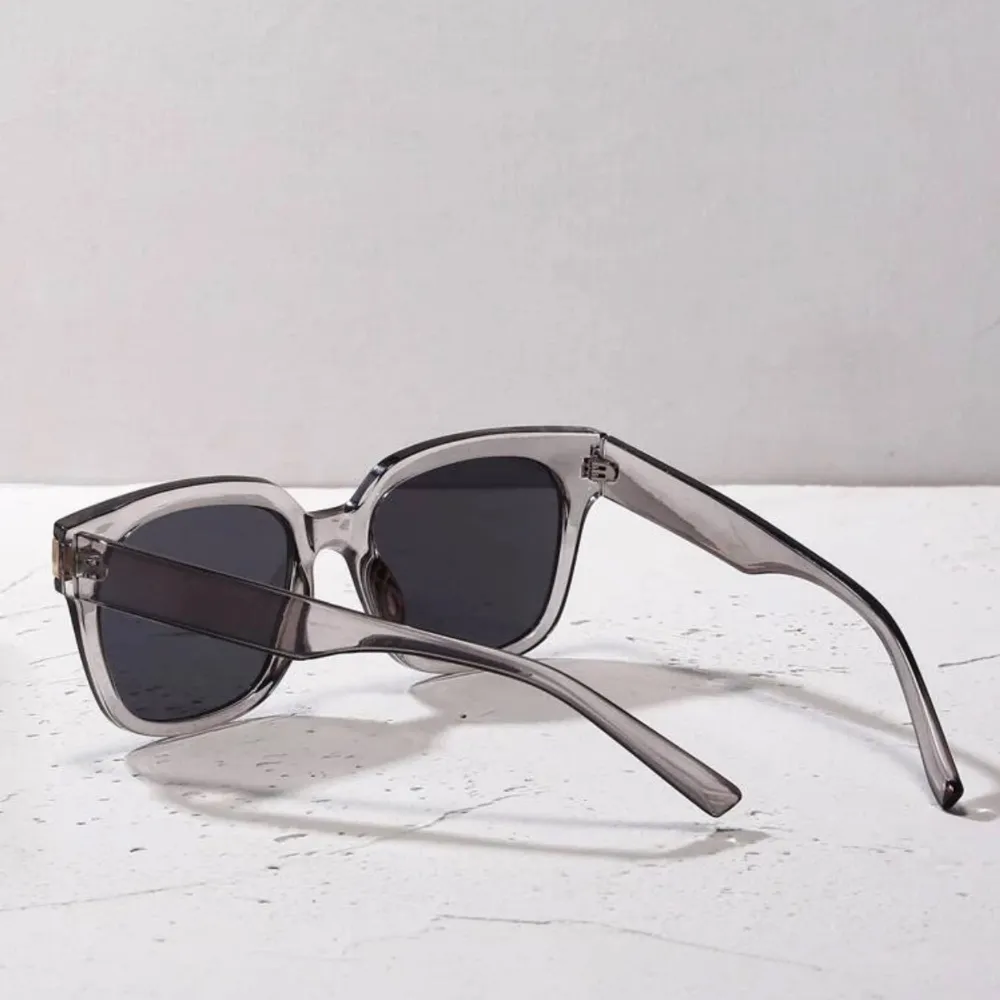 Snygga solglasögon med transparent båge och mörka linser. Den fyrkantiga formen ger en modern look och de är perfekta för soliga dagar. En stilren accessoar som passar till många outfits.. Asusteet.
