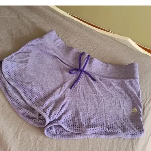 Lila träningsshorts från Adidas - Lila shorts från Adidas med små prickar och snörning i midjan. Perfekta för träning eller varma dagar. Adidas-logga på ena benet. Köparen står för frakten ✨️
