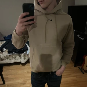 Beige hoodie från Nike - Säljer en beige hoodie från Nike med klassisk logga på bröstet. Tröjan har huva med dragsko och en stor magficka. Perfekt för en avslappnad stil.
