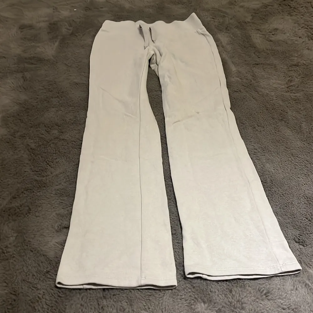 Säljer ett par ljusgrå mjukisbyxor från H&M med bred resår i midjan och dragsko. Byxorna har raka ben och är tillverkade i mjuk bomullsmix, perfekta för en avslappnad stil.. Farkut & Housut.