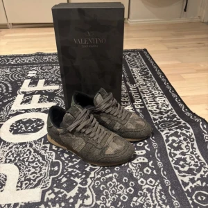 Valentino Rockrunner sneakers i camouflage - Säljer ett par Valentino Rockrunner sneakers i grön och brun camouflage med snörning och gummisula. Skorna har klassisk rund tå och är tillverkade i en mix av mocka och skinn. Perfekta för dig som vill ha något unikt och stilrent från Valentino Garavani.