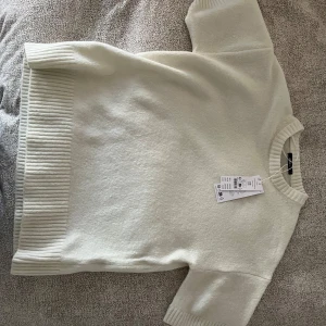 Vit stickad kortärmad tröja från Gina Tricot - Säljer en vit stickad tröja från Gina Tricot med korta ärmar och bred ribbad kant vid ärmslut, halsringning och nederkant. Perfekt till sommaren. Aldrig använd pga att den är för lång och prislapp finns kvar, köpt för 400kr 🥰