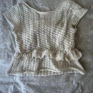 Vit virkad topp med volang från Zara - Säljer en söt vit virkad topp från Zara med korta ärmar och volangdetalj i midjan. Perfekt för en somrig look och lätt att matcha med jeans eller kjol.