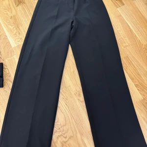 Svarta kostymbyxor från ONLY - Snygga svarta kostymbyxor från ONLY med klassisk rak passform och hög midja. Byxorna har vida ben och är perfekta för en stilren look. Tillverkade i ett mjukt och följsamt material som känns bekvämt hela dagen.