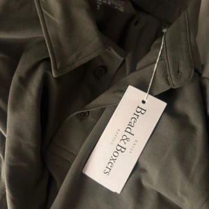 Olivgrön pikétröja från Bread & Boxers - Säljer en olivgrön pikétröja från Bread & Boxers i storlek S. Tröjan har klassisk krage, knappar framtill och långa ärmar. Tillverkad i mjuk bomull som känns skön mot huden. Perfekt för en stilren och avslappnad look.